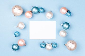 Frame of Christmas balls with blank card mockup on blue background. Holiday background, top view.