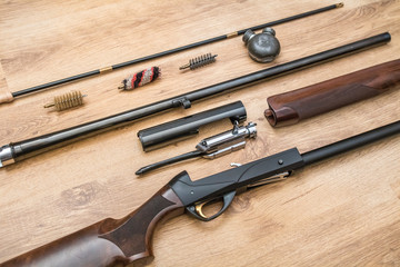 disassembled shotgun parts and cleaning kit on the wooden background