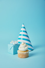 party hat, gift box and tasty cupcake with sugar sprinkles on blue background