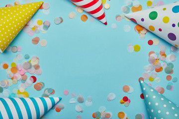 Obraz premium Top view of party hats and confetti on blue background