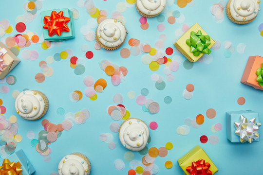 Top view of tasty cupcakes, confetti and gifts on blue background