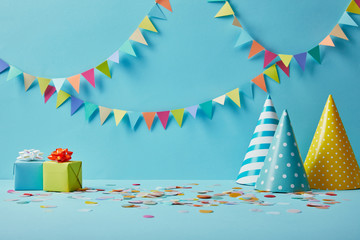 party hats, confetti and gifts on blue background with colorful bunting