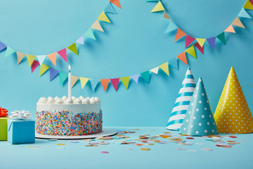 Delicious birthday cake, gifts, party hats and confetti on blue background with bunting - obrazy, fototapety, plakaty