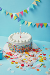 Tasty cake with sugar sprinkles and confetti on blue background with colorful bunting