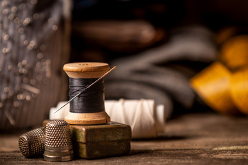 Close-up view of beautiful wooden sewing spool with thin black thread and needle placed on rough wooden plank table with defocused tape measure on background