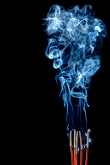 Closeup of calmly burning incense sticks with blue fume on black background