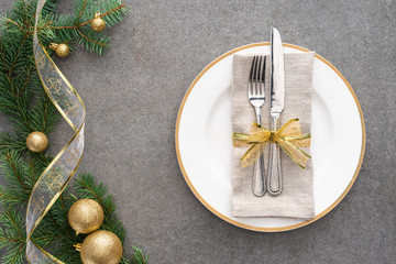 elevated view of served table with plate, fork and knife wrapped by festive ribbon near branch decorated by golden christmas balls