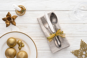 view from above of plate with golden christmas balls, candle and fork, spoon, knife wrapped by ribbon on wooden table