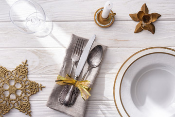 top view of wine glass, plate with golden christmas balls, candle and fork, spoon, knife wrapped by ribbon on wooden table