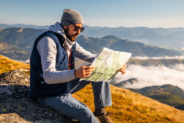 Hipster young man holding in hands and looking on map on mountain background