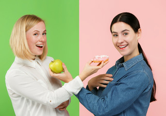 Diet. Dieting concept. Healthy useful food. Beautiful young women choosing between fruits and unhelathy cake at studio. Human emotions and comparison concepts