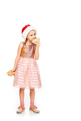 adorable little child in santa hat eating ginger cookies and looking at camera isolated on white