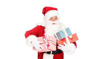 santa claus holding pile of gift boxes and looking at camera with shocked expression isolated on white