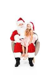 santa claus and little child sitting in armchair together and looking at camera isolated on white