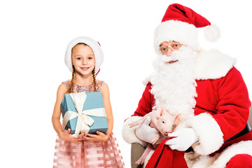 santa claus and little child looking at camera while holding piggy and gift box isolated on white