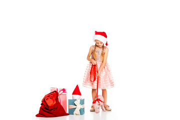 adorable little child in santa hat with leashed piggy and pile of christmas gifts isolated on white