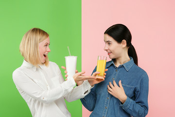 Diet. Dieting concept. Healthy useful food. Beautiful young women choosing between fruit orange juice and unhelathy carbonated sweet drink from fast food at studio. Human emotions and comparison