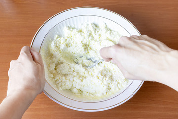 Cropped female hands mix cottage cheese in a bowl