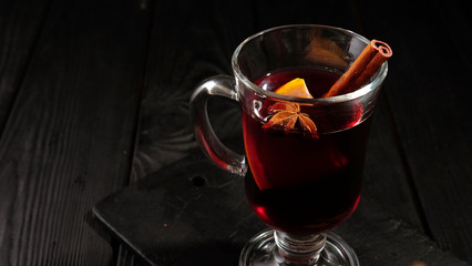closeup glass of mulled wine with orange and cinnamon on dark black background
