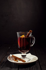 closeup glass of mulled wine with orange and cinnamon on dark black background, on white plate