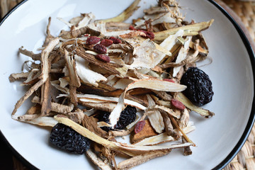 Chinese traditional medicine script. Herbal tea with jujubes, goji berries, gingseng roots and others on white plate on neutral background. Side and top view.