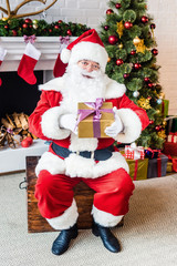 happy santa claus holding christmas present and looking at camera