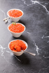 Red caviar Three species of salmon caviar in a white bowl on a black marble background. Variety of tastes.Seafood. Healthy Food Concept. Snack.Copy space for Text.