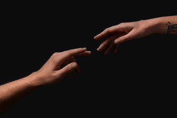 Male and female hands reaching out to each other on dark background