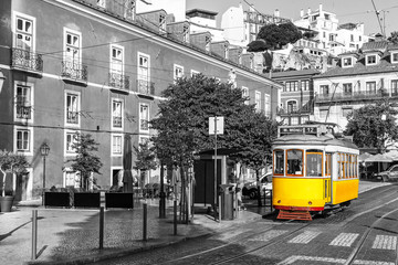 Yellow tram on old streets of Lisbon, Alfama, Portugal, popular touristic attraction and destination. Black and white picture with a coloured tram. - obrazy, fototapety, plakaty