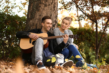 Fototapeta premium Handsome young man with guitar and his beloved resting in autumn park
