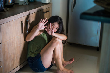 young scared and helpless Asian Chinese woman horrified suffering domestic violence victim of abuse from drunk alcoholic husband at home kitchen floor crying