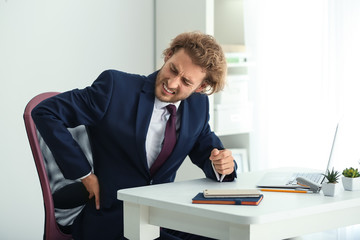 Young businessman suffering from back pain in office