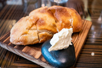 Freshly baked bread right from oven on a wooden tray with butter for appetizer or meal starter. Looks tasty and delicious. Good source of carbohydrate. Not gluten-free. Natural light. Selective Focus.
