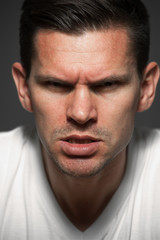 Fototapeta premium Portrait close-up of caucasian handsome angry wild man with clenched teeth dressed in a white t-shirt looking at the camera