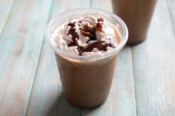 Cold coffee covered with whipped cream and chocolate in wet plastic cup on wooden table