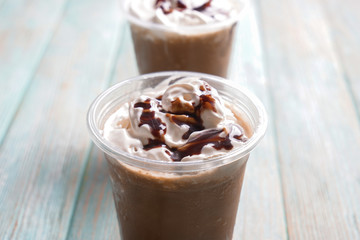 Cold coffee covered with whipped cream and chocolate in wet plastic cups on wooden table, closeup