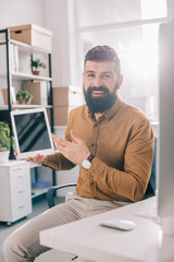 adult business man looking at camera and presenting digital tablet with blank screen at workplace with backlit