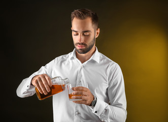 Businessman pouring whiskey into glass on dark background