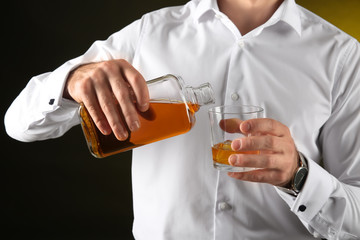 Businessman pouring whiskey into glass on dark background, closeup