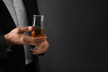 Elderly businessman with glass of whiskey on dark background, closeup
