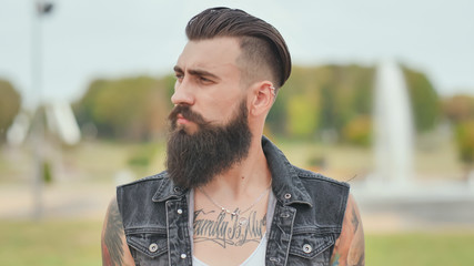 Portrait of a brutal and bearded man with tattoos on his shoulders.