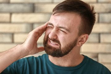 Man suffering from headache against brick wall
