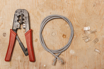 cable crimping tool, twisted pair cable and plugs lie on a wooden surface top view