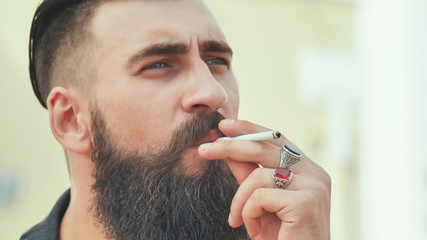 A bearded man smokes a cigarette in the street.