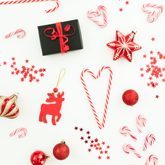Christmas composition. Surprise gift, red toys, candy canes and confetti on white background. Flat lay, top view.