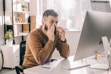 sick businessman sitting at office desk with runny using nasal spray
