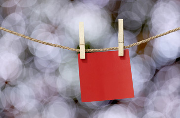 Blank red paper notes hanging on clothesline for design in Christmas Day on bokeh light background.