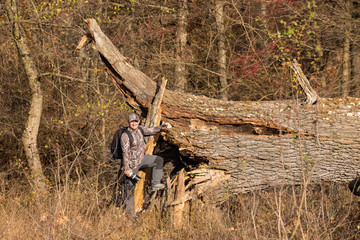 A man in a camouflage suit next to an old oak fallen after the storm