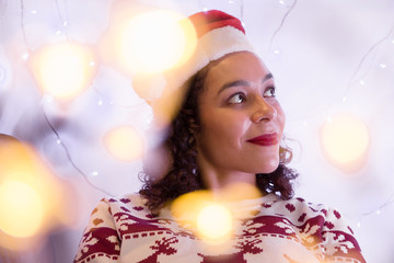 Dreamy woman with Santa Claus hat and Christmas sweater at home. blurred bokeh lights.