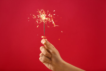 Female hand with Christmas sparkler on color background